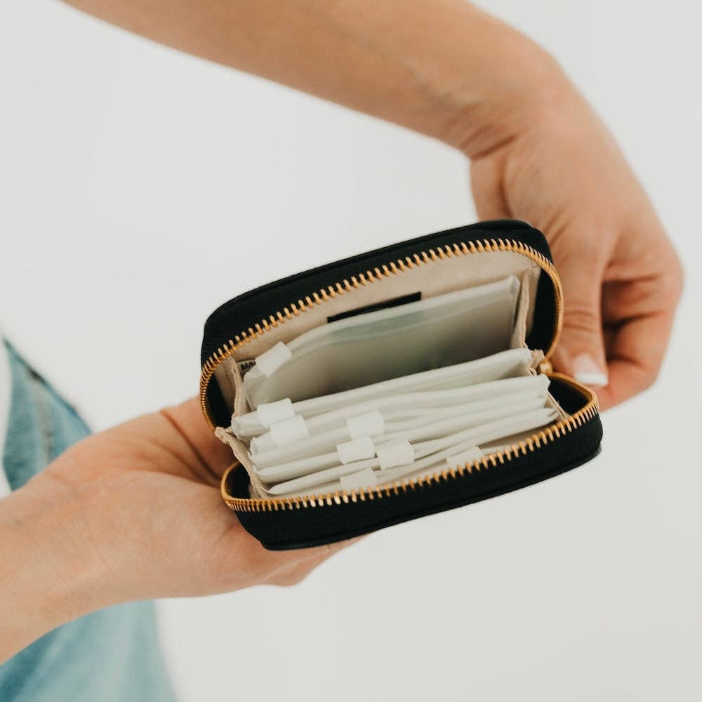 Small black zippered case with white items held by a person against a neutral background