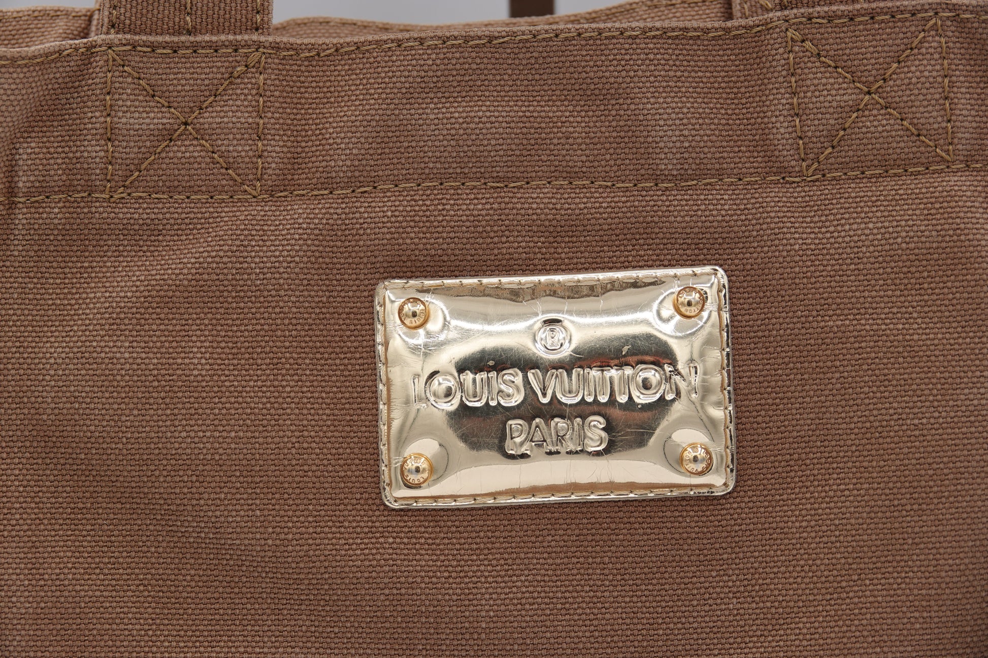 Close-up of a Louis Vuitton bag with a gold tag on a brown background