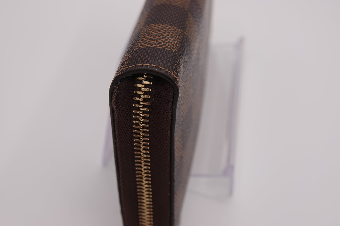 Close-up of a brown checkered wallet with a gold zipper on a white background