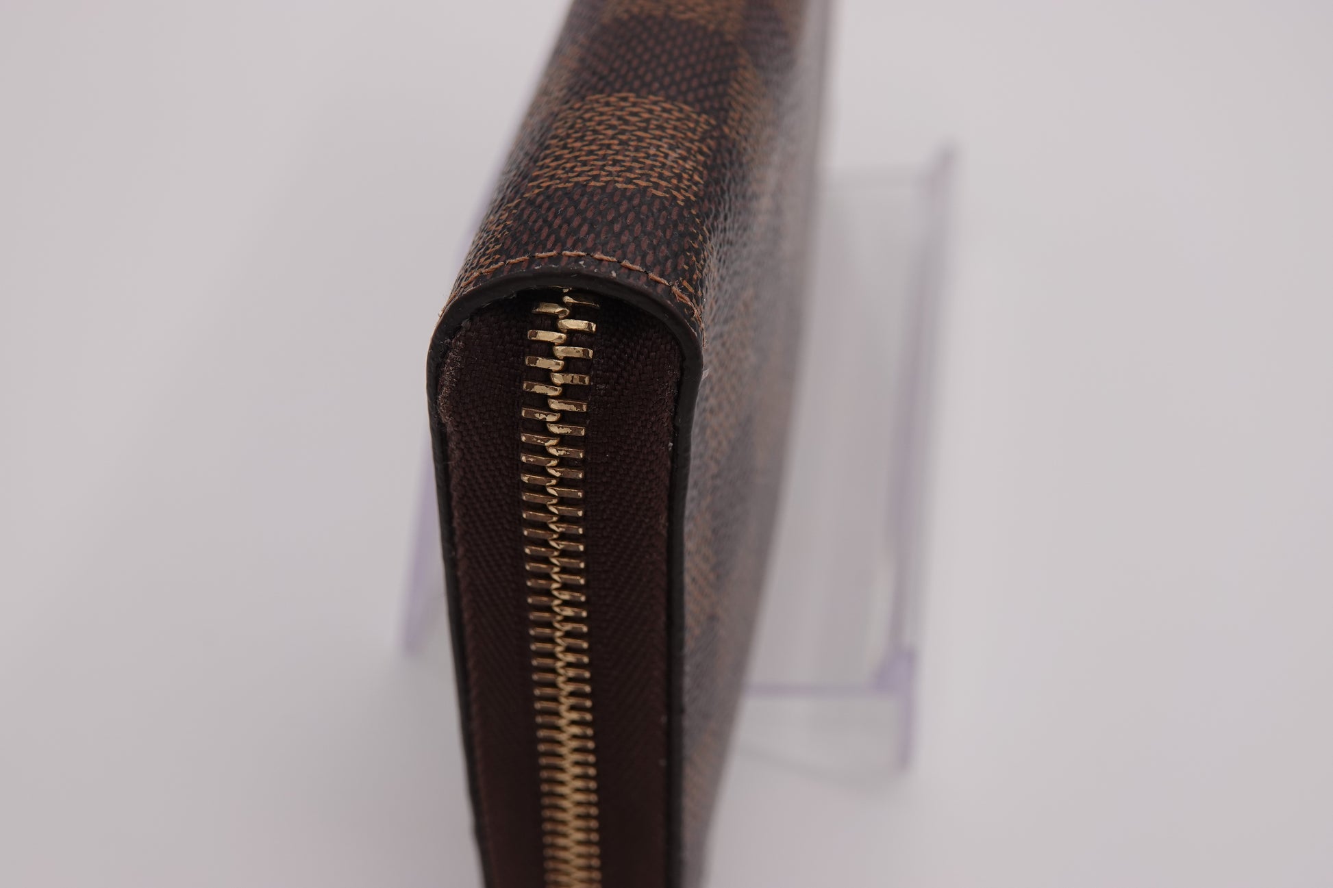 Close-up of a brown checkered wallet with a gold zipper on a white background