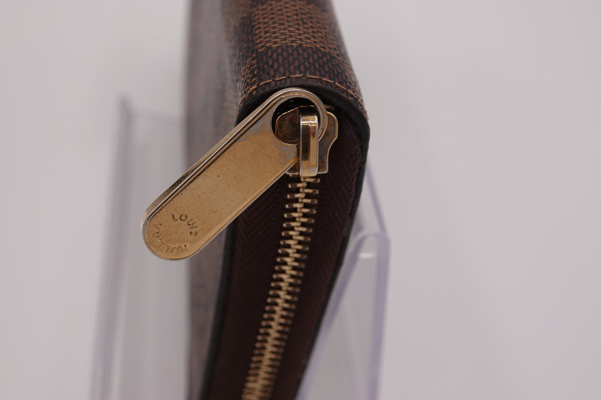 Close-up of a brown leather wallet with gold zipper pull on a light gray background