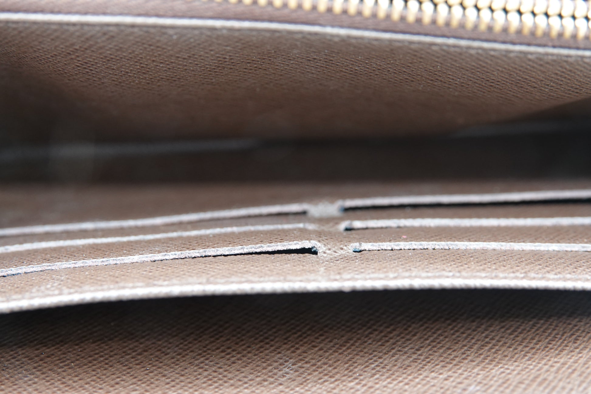 Close-up of a brown leather bag with visible stitching and a gold zipper.