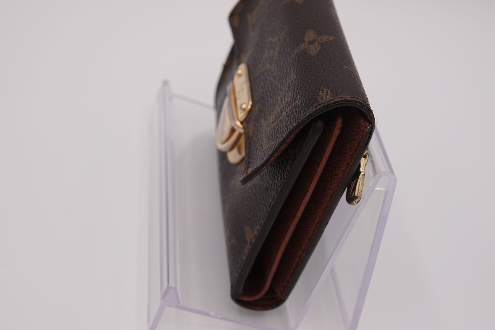 Brown wallet with gold accents on a clear stand against a white background