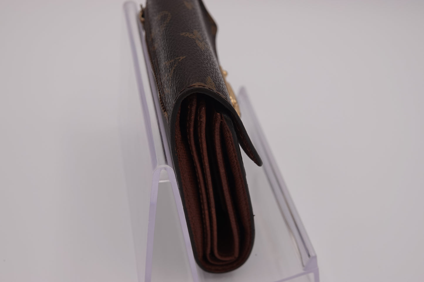 Brown wallet with visible brand logo on a clear stand against a white background