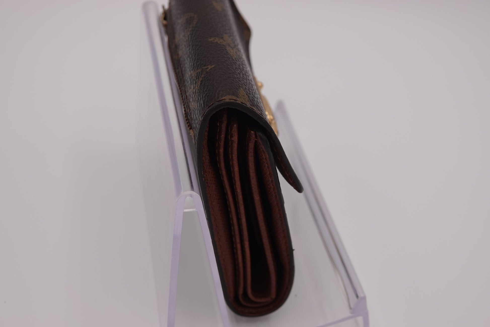 Brown wallet with visible brand logo on a clear stand against a white background