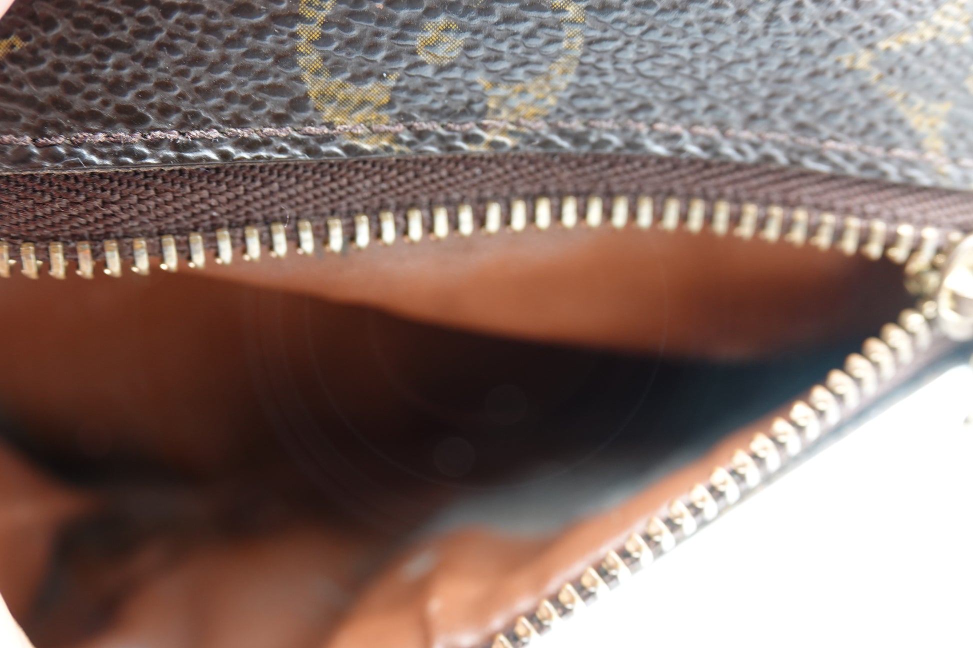 Close-up of a brown leather bag with gold zipper and patterned background