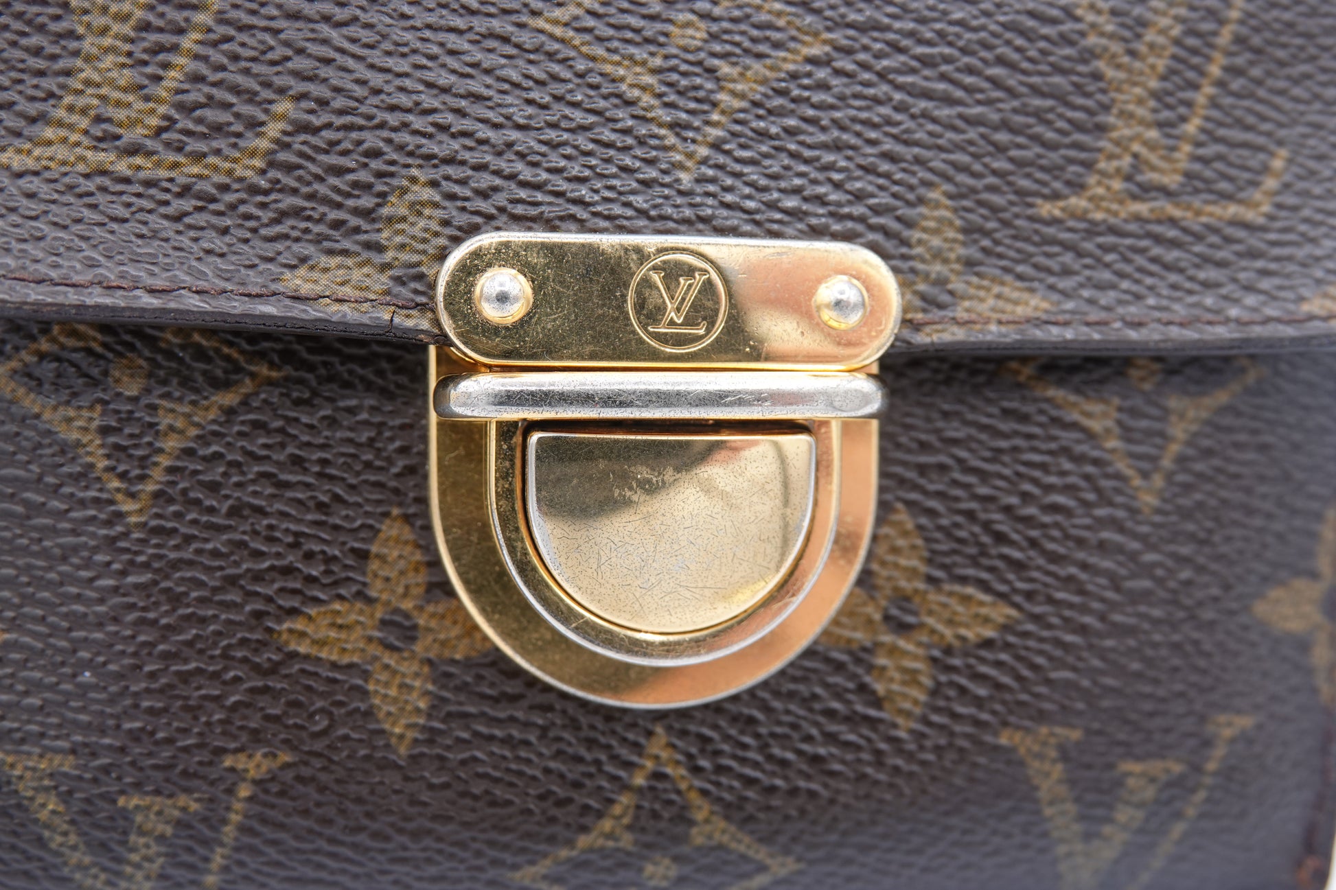 Close-up of a gold and silver metal clasp on a Louis Vuitton bag with monogram pattern.