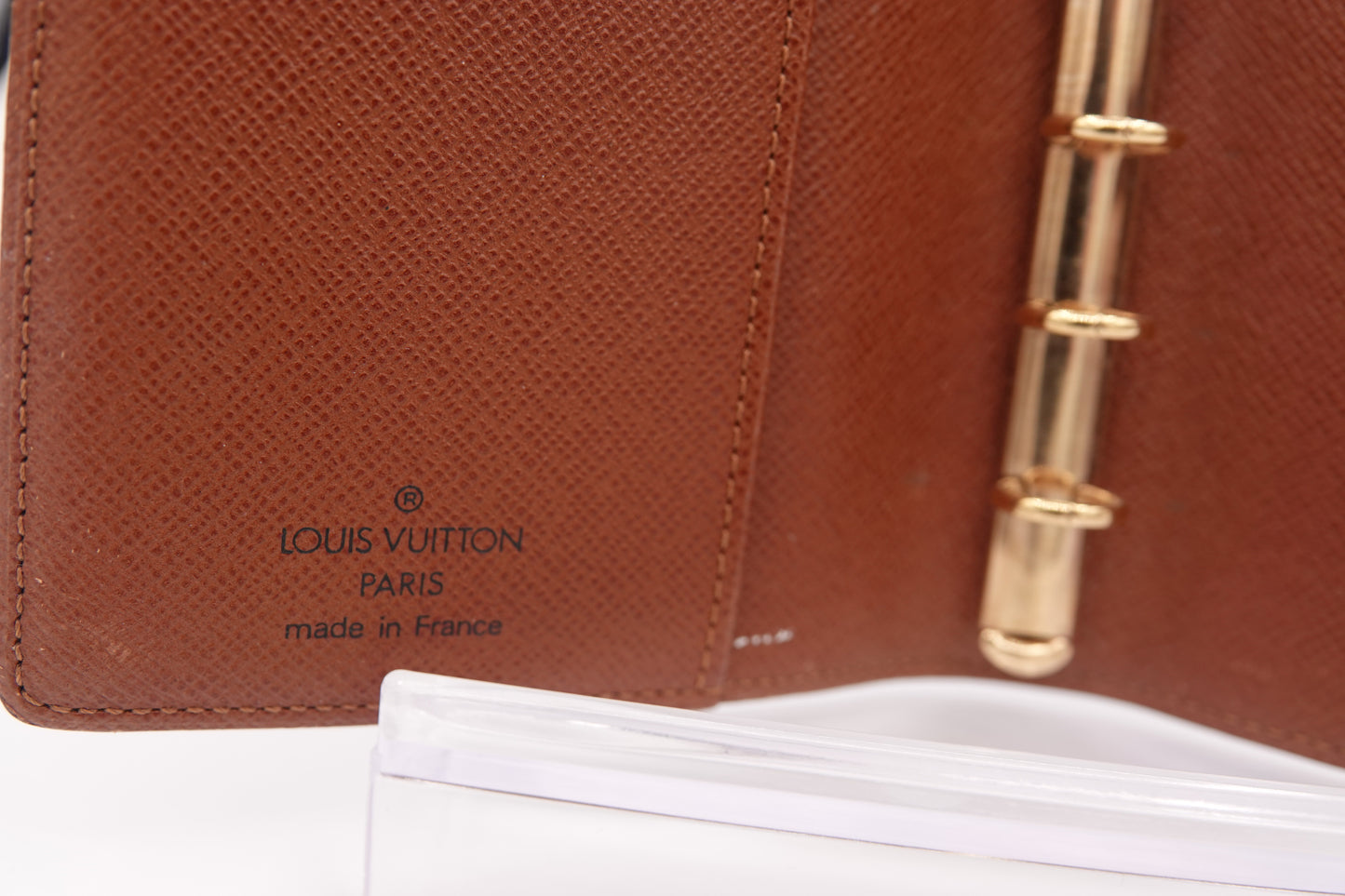 Brown leather Louis Vuitton planner with gold binding on a white background
