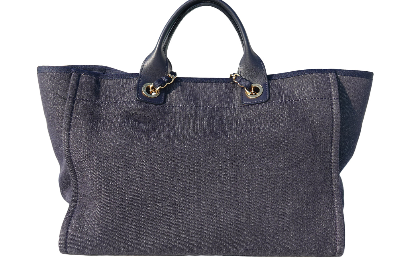 Dark blue tote bag with gold hardware on a reflective surface near a pool.