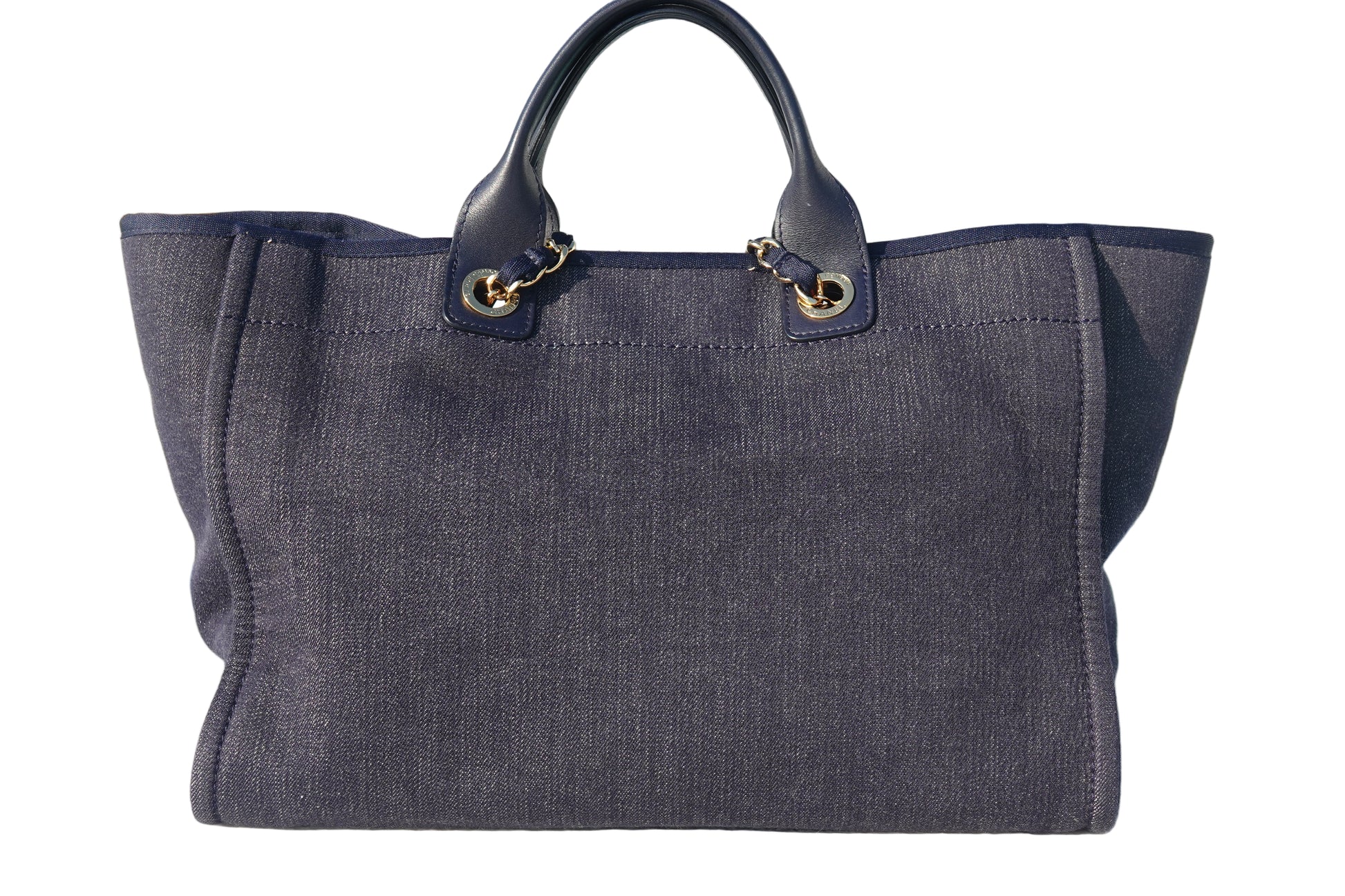 Dark blue tote bag with gold hardware on a reflective surface near a pool.