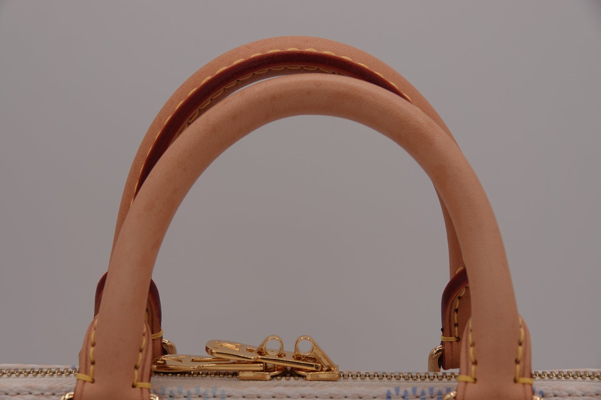 Close-up of a brown leather handbag handle with gold hardware on a gray background