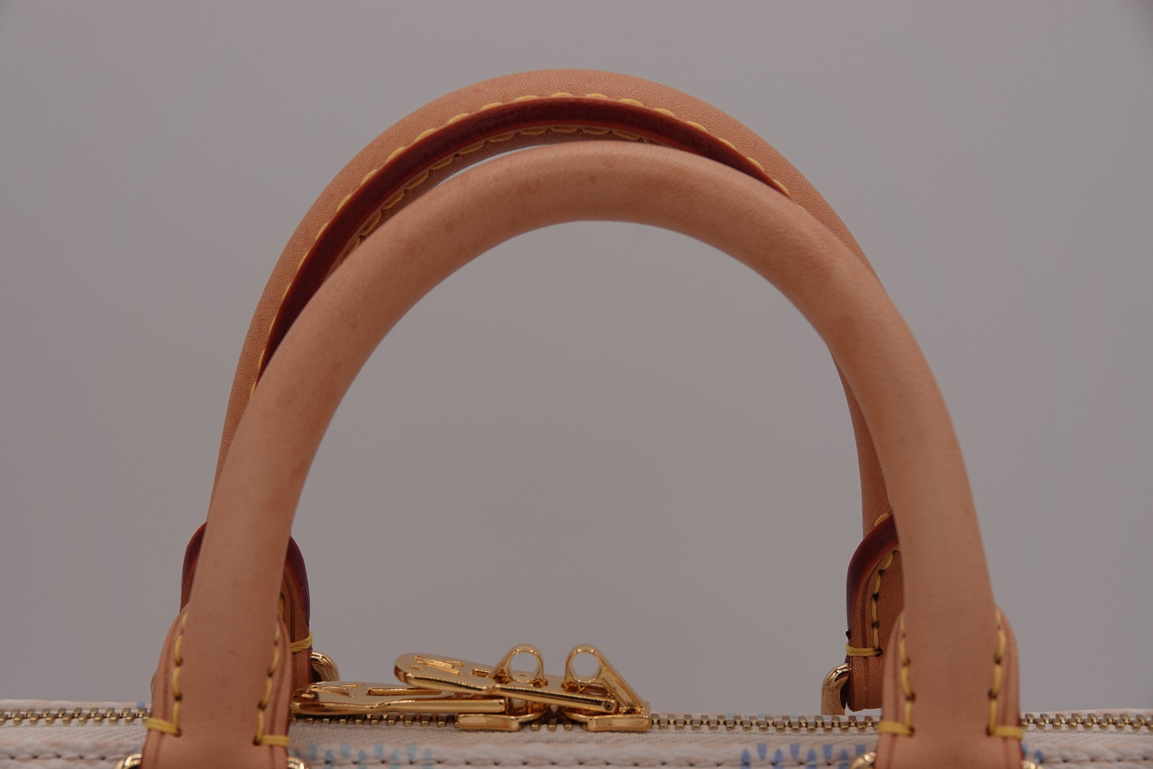 Close-up of a brown leather handbag handle with gold hardware on a gray background