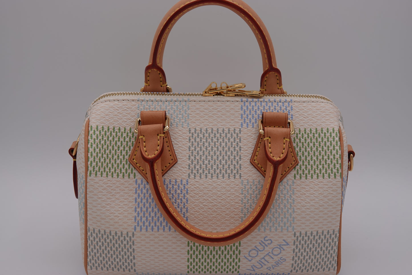 Designer handbag with checkered pattern and brown leather handles on a gray background