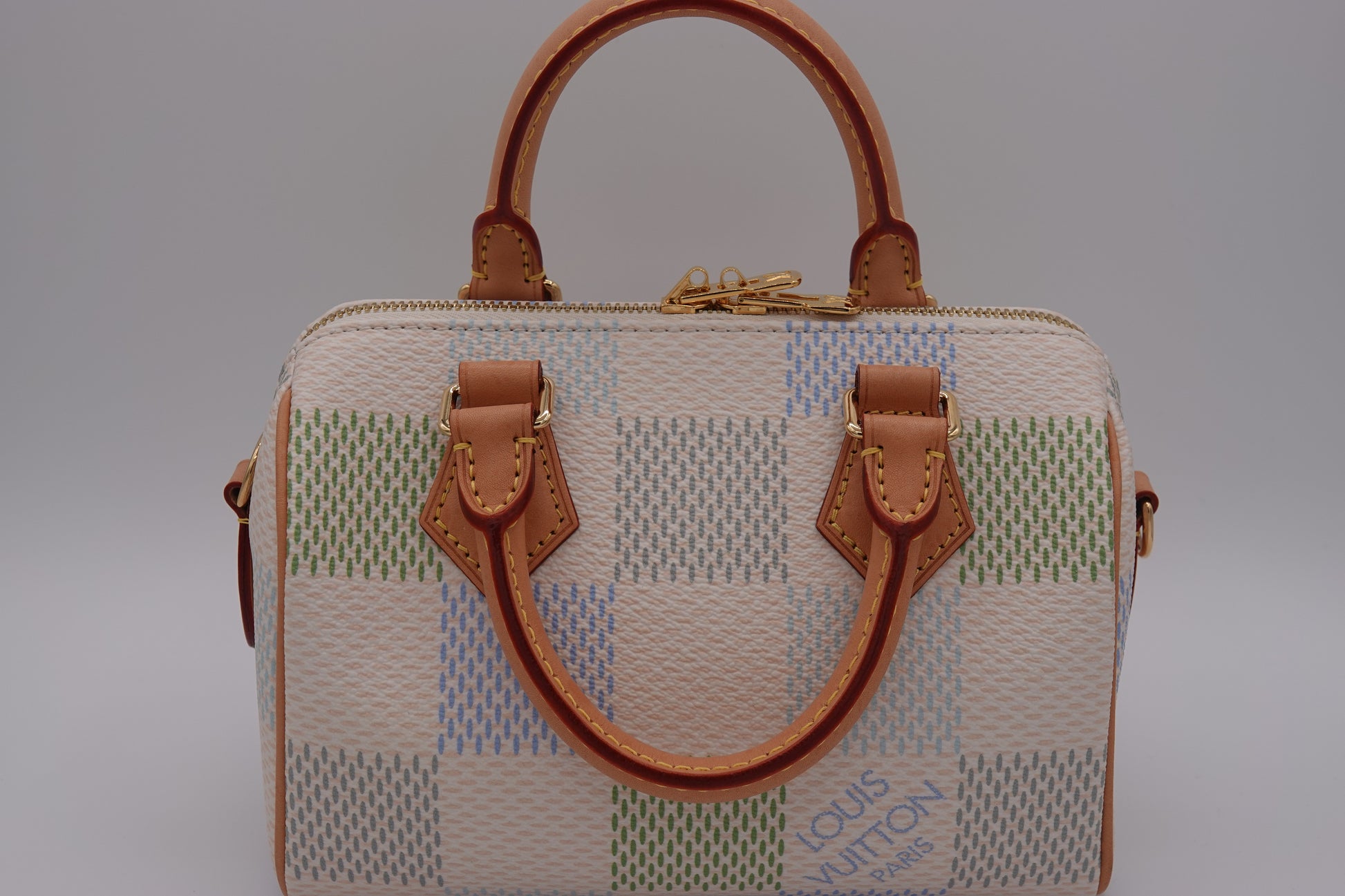 Designer handbag with checkered pattern and brown leather handles on a gray background