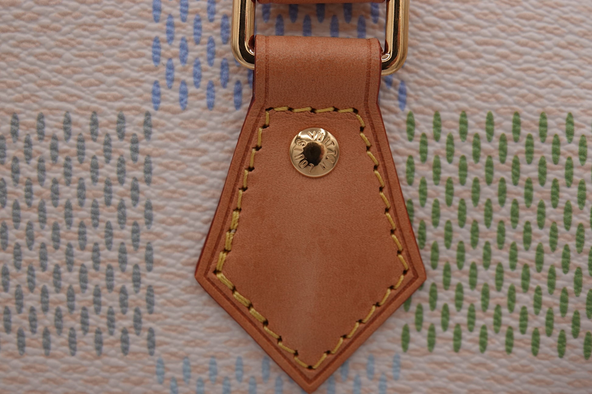 Close-up of a brown leather tag with gold stitching on a patterned fabric background