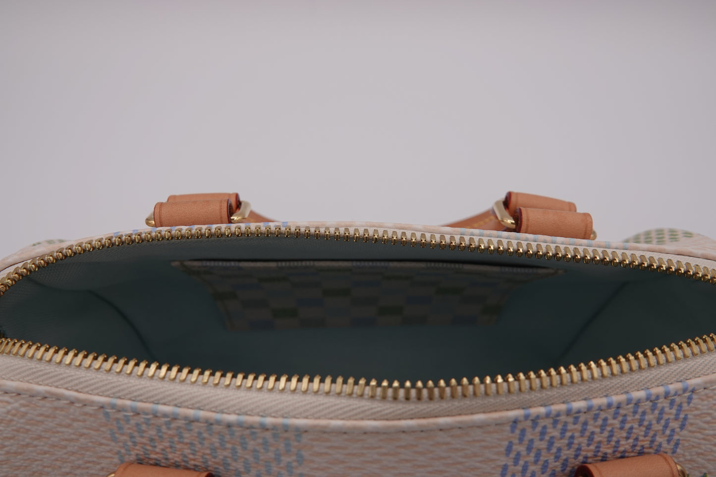 Close-up of a patterned handbag with a zipper and brown handles on a light gray background.