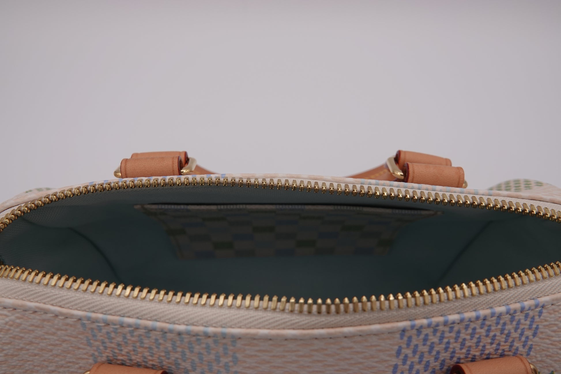 Close-up of a patterned handbag with a zipper and brown handles on a light gray background.