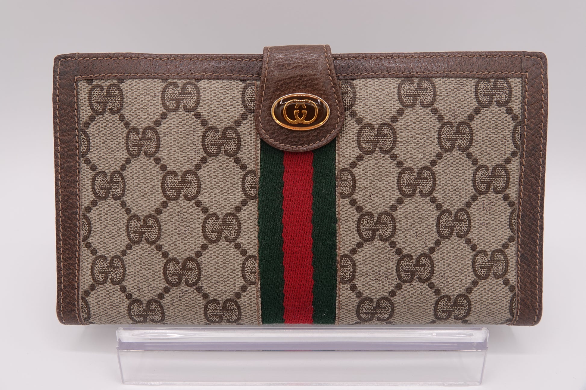 Gucci wallet with brown monogram canvas and red and green striped detail on a white background