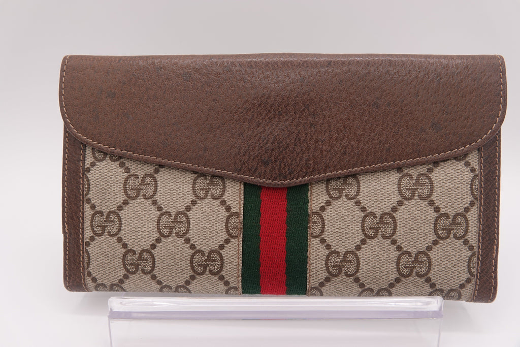 Gucci wallet with brown leather flap and patterned fabric body on a white background