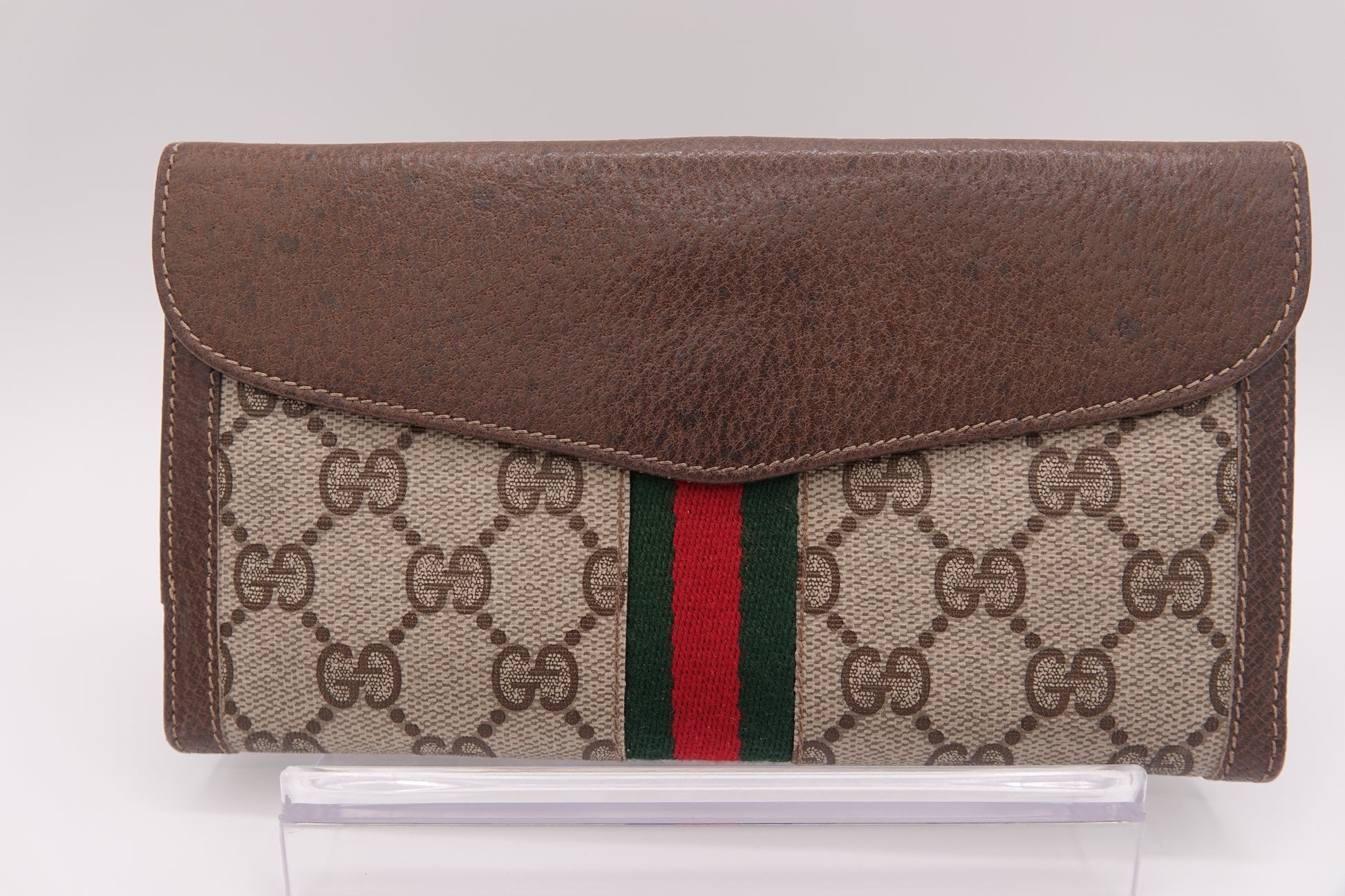 Gucci wallet with brown leather flap and patterned fabric body on a white background