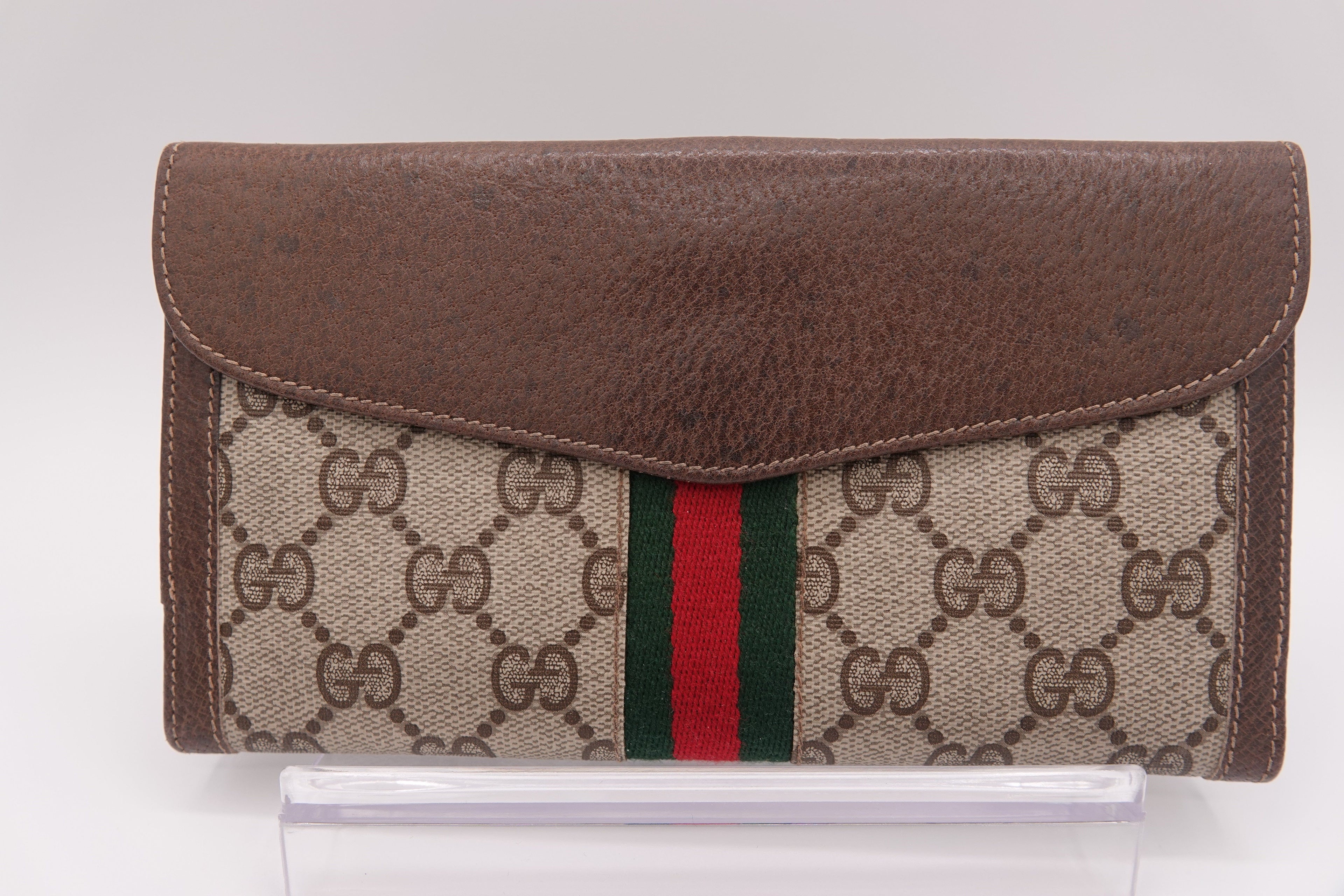 Gucci wallet with brown leather flap and patterned fabric body on a white background