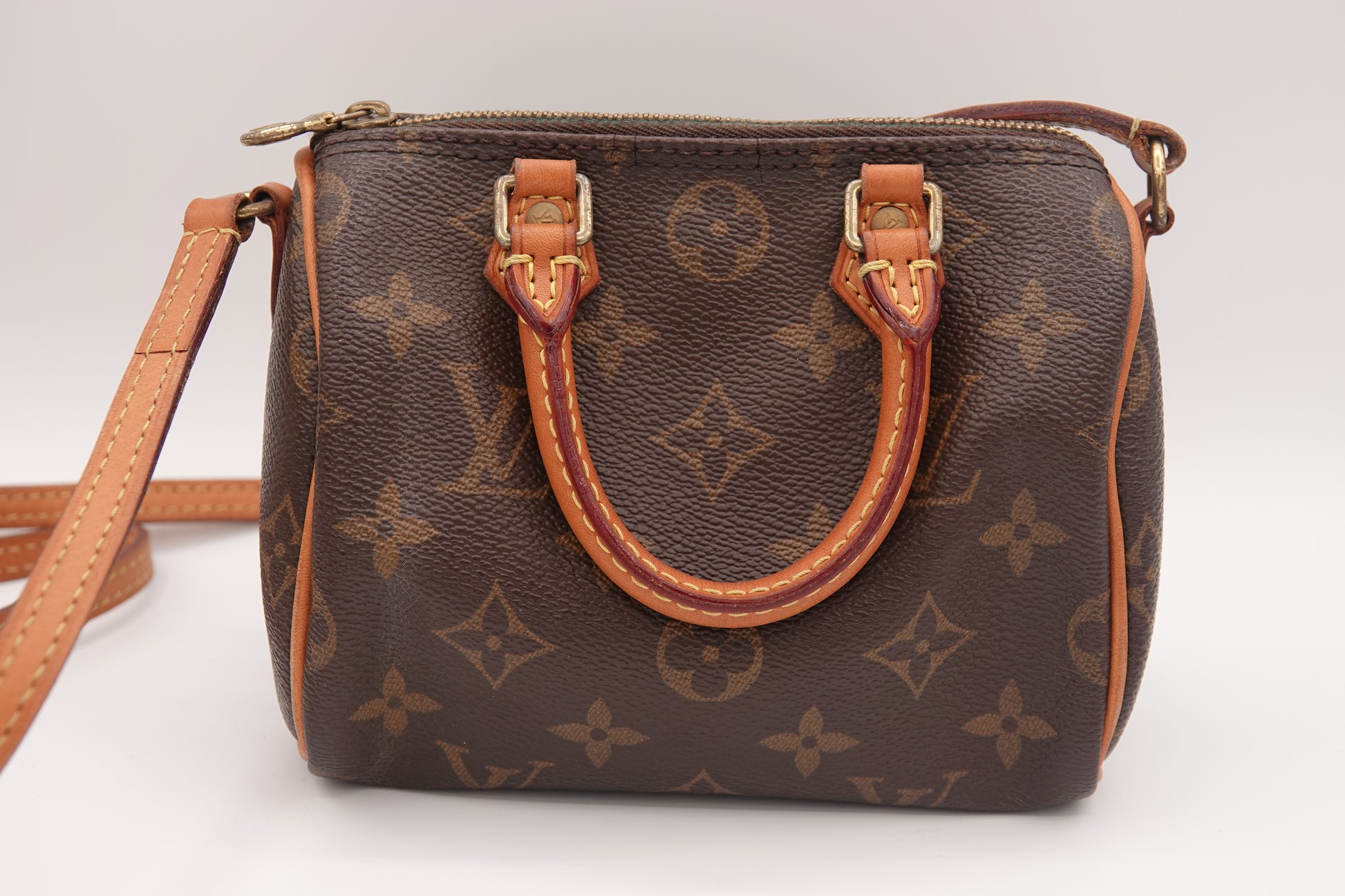 Brown handbag with tan leather handle and strap on a white background