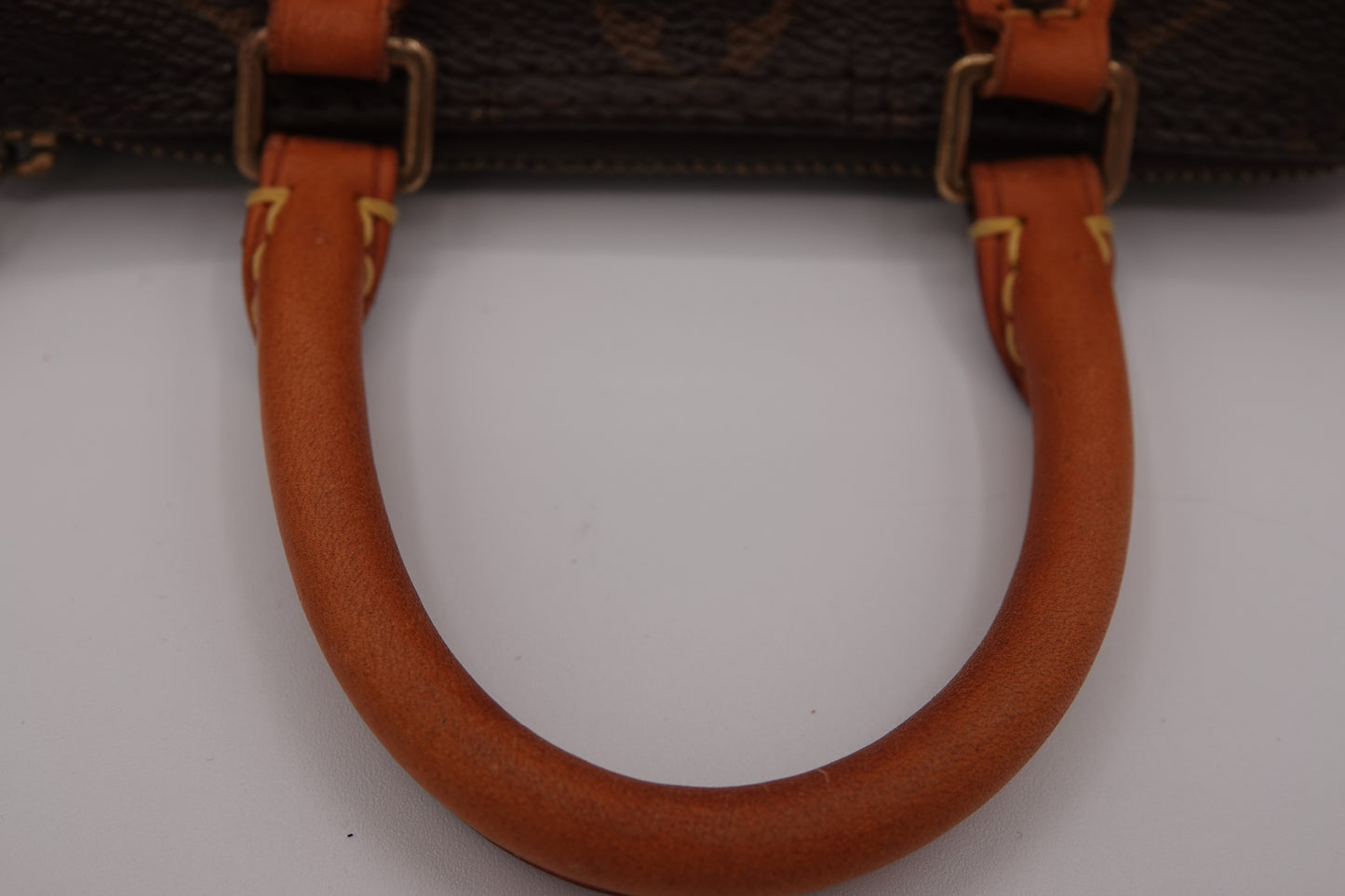 Close-up of a brown leather handbag handle with gold hardware on a white background