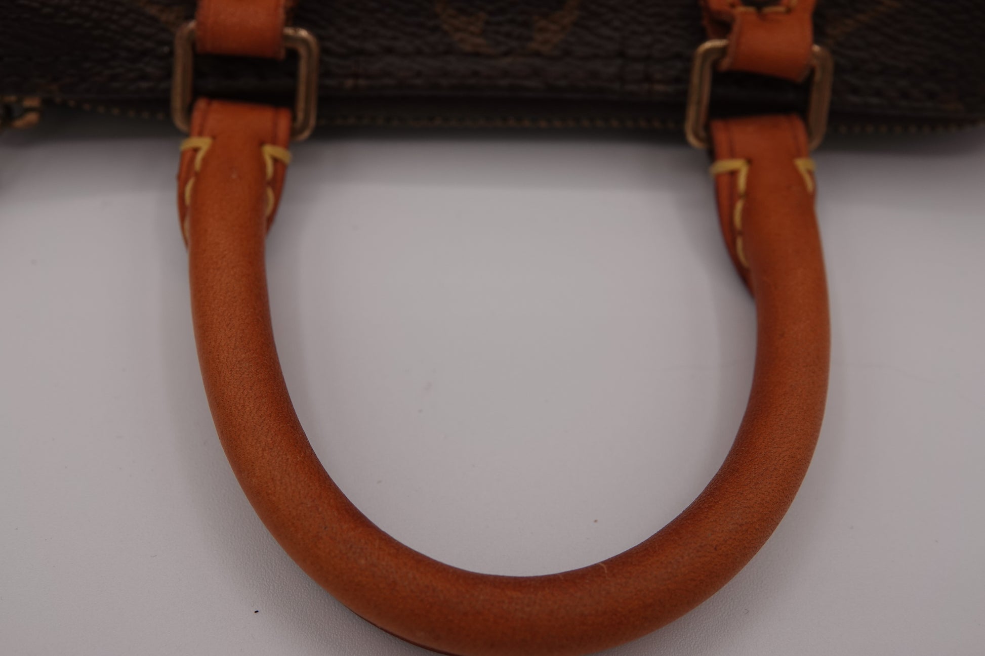 Close-up of a brown leather handbag handle with gold hardware on a white background