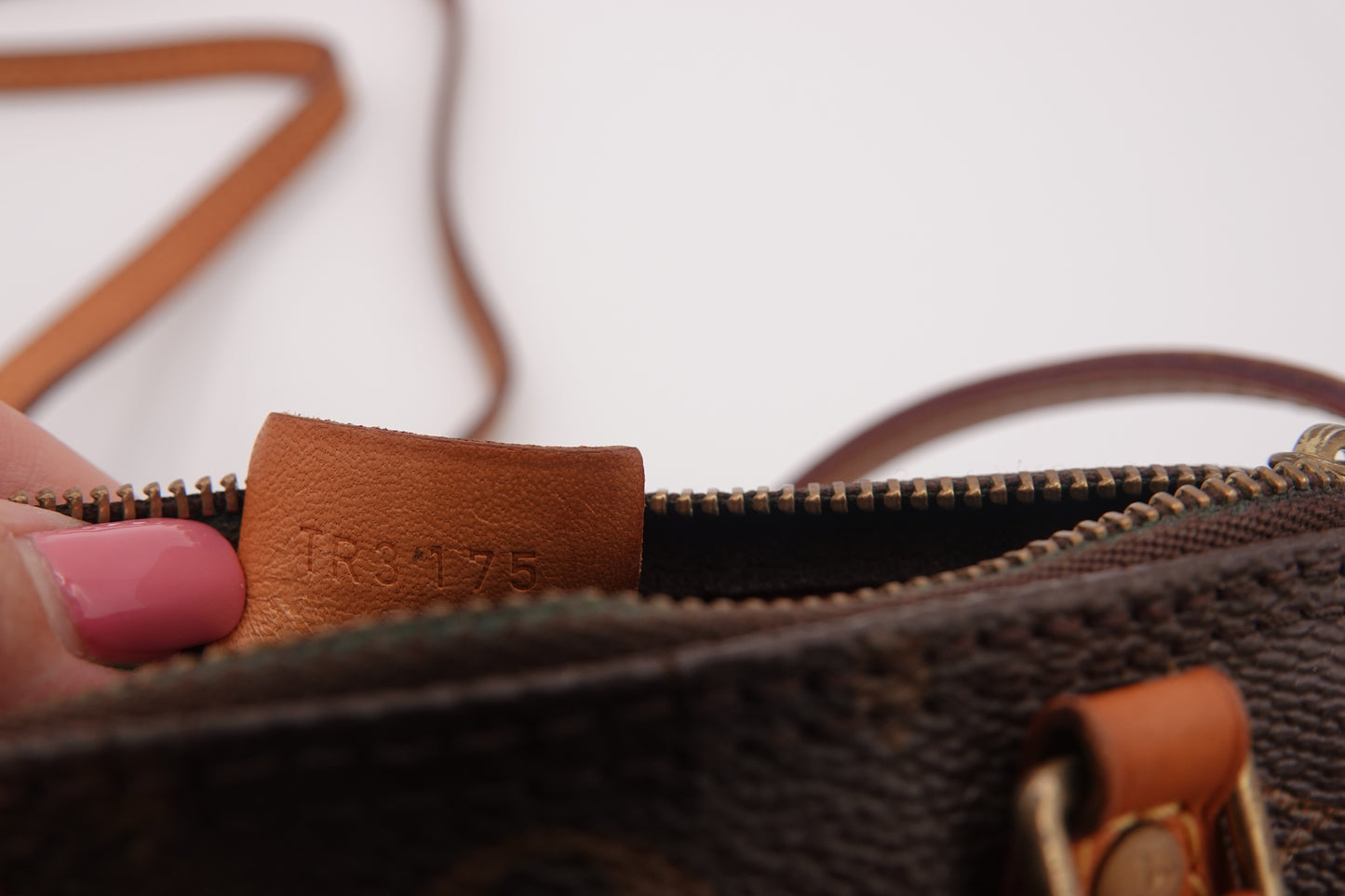 Close-up of a brown leather zipper with 'LOUIS VUITTON' branding on a blurred background.