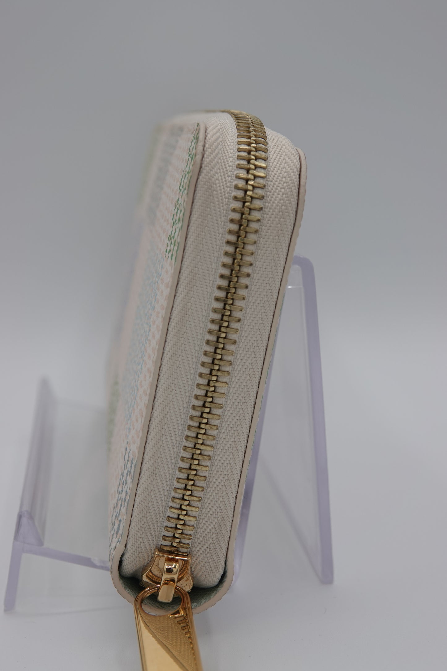 Beige pouch with gold zipper on a clear stand against a white background