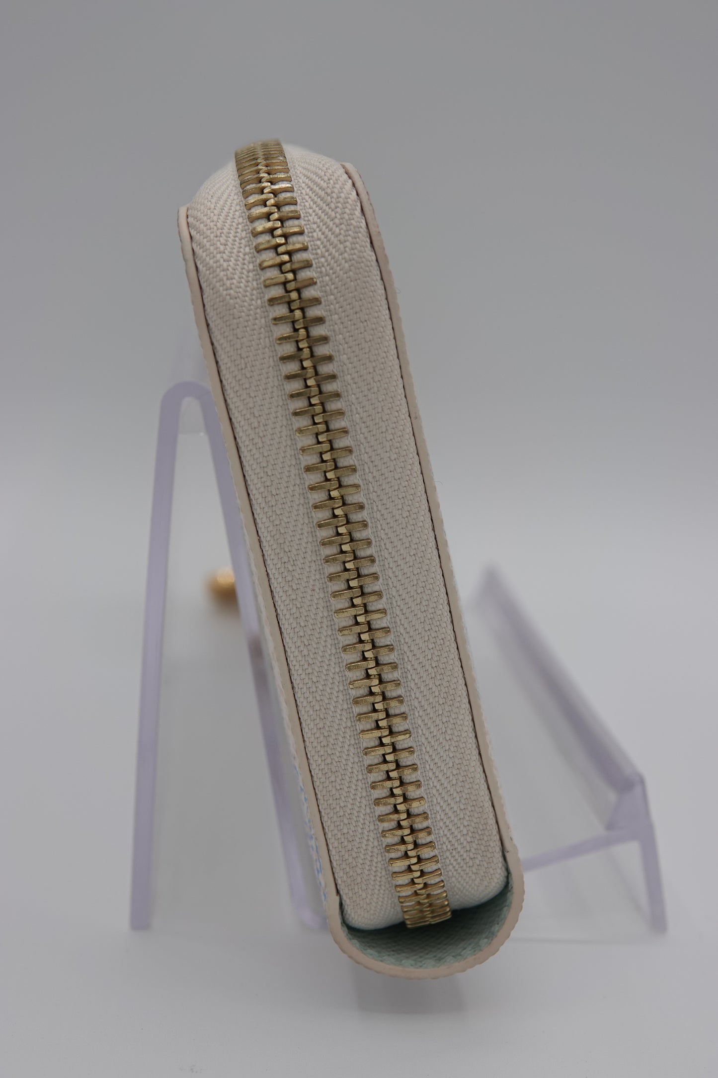 Beige fabric with a gold zipper on a clear stand against a light gray background
