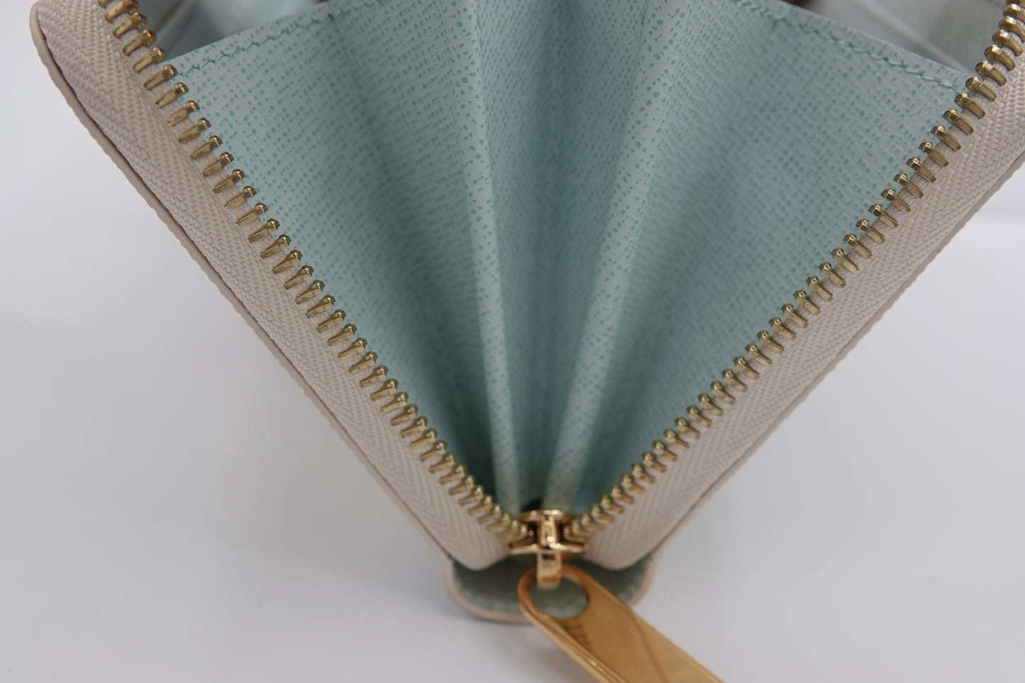 Close-up of a green and beige zippered pouch with gold zipper on a white background