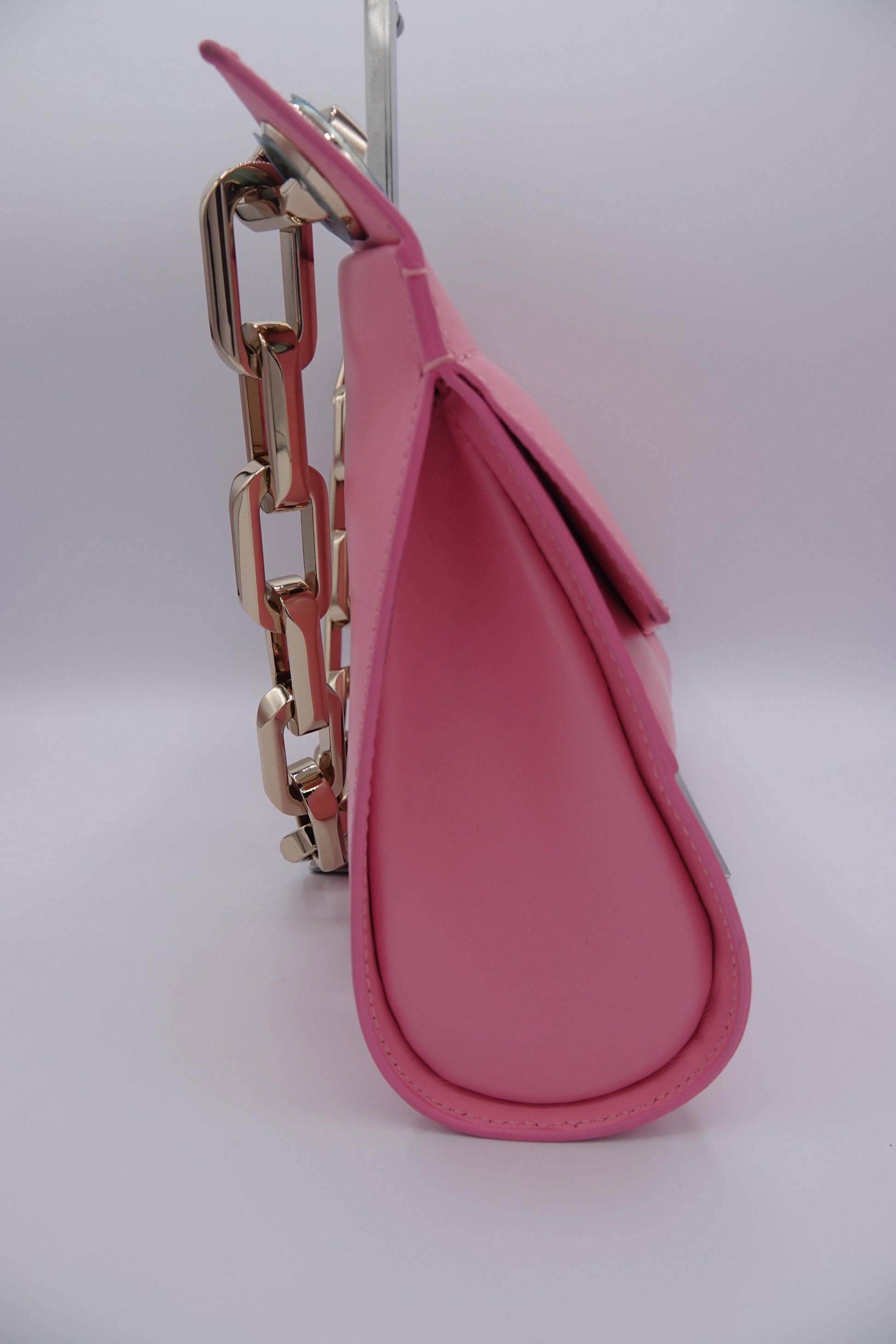 Pink leather handbag with gold chain detail on a white background