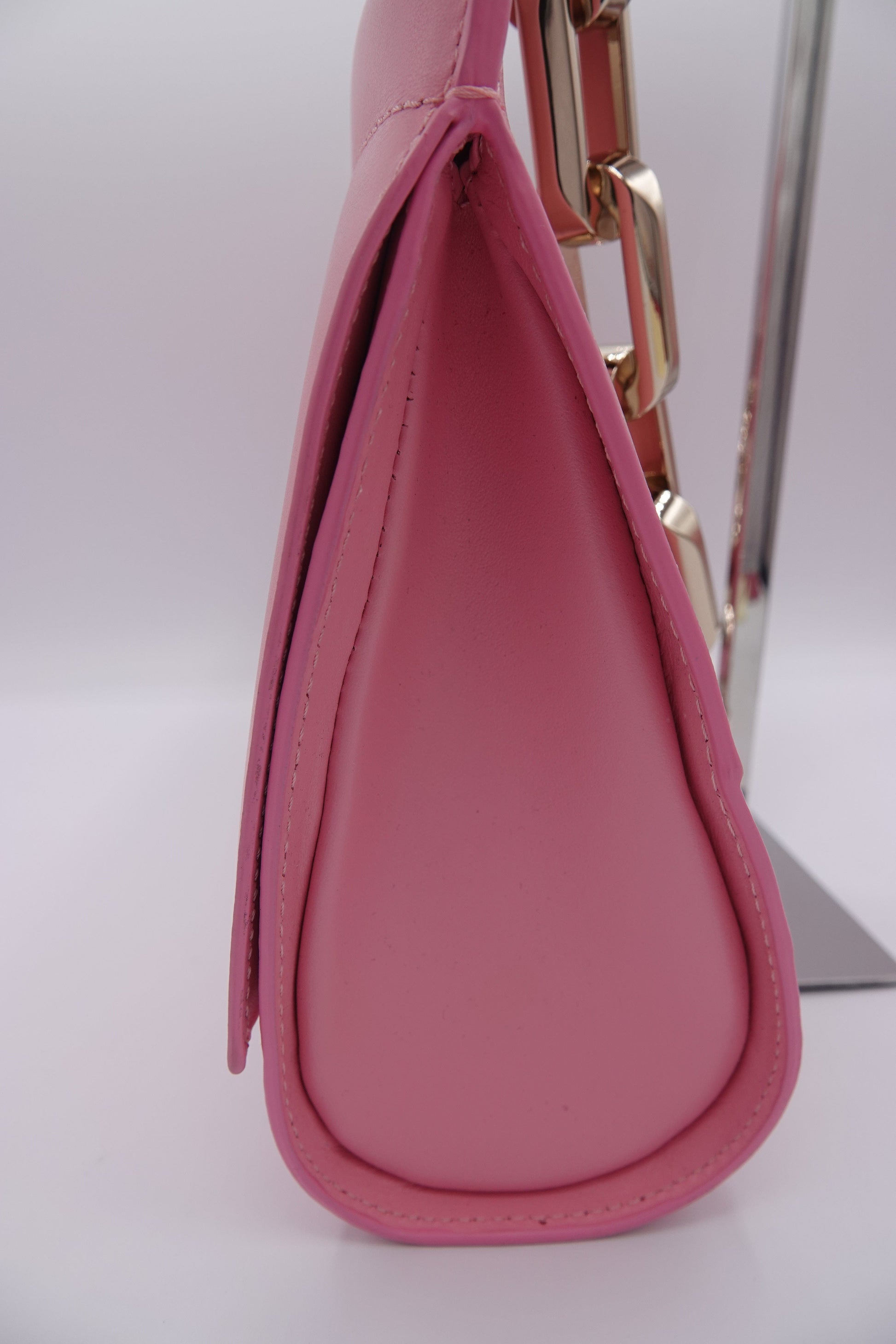 Close-up of a pink handbag with gold accents on a white background