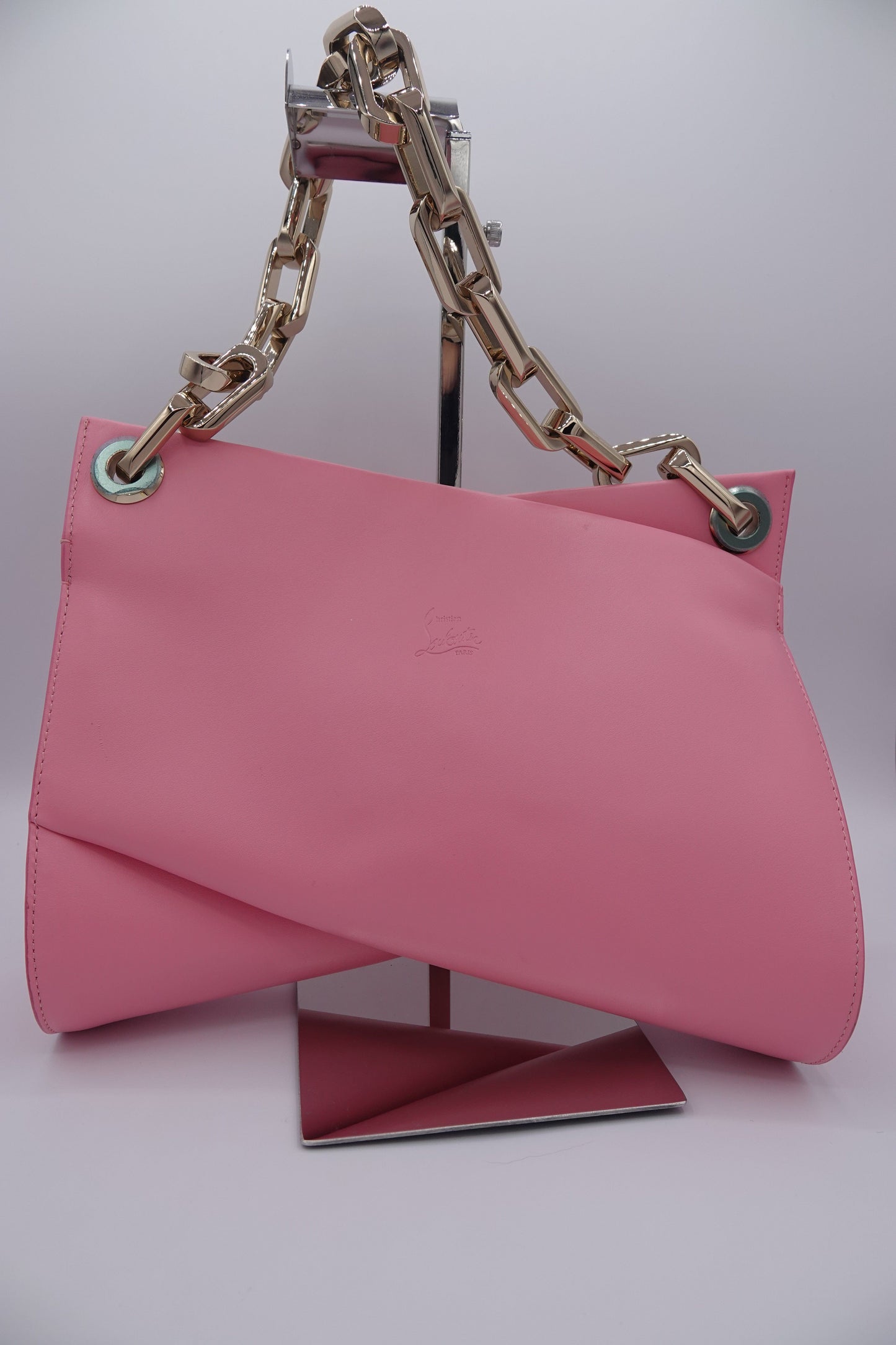 Pink handbag with gold chain handle on a light pink background