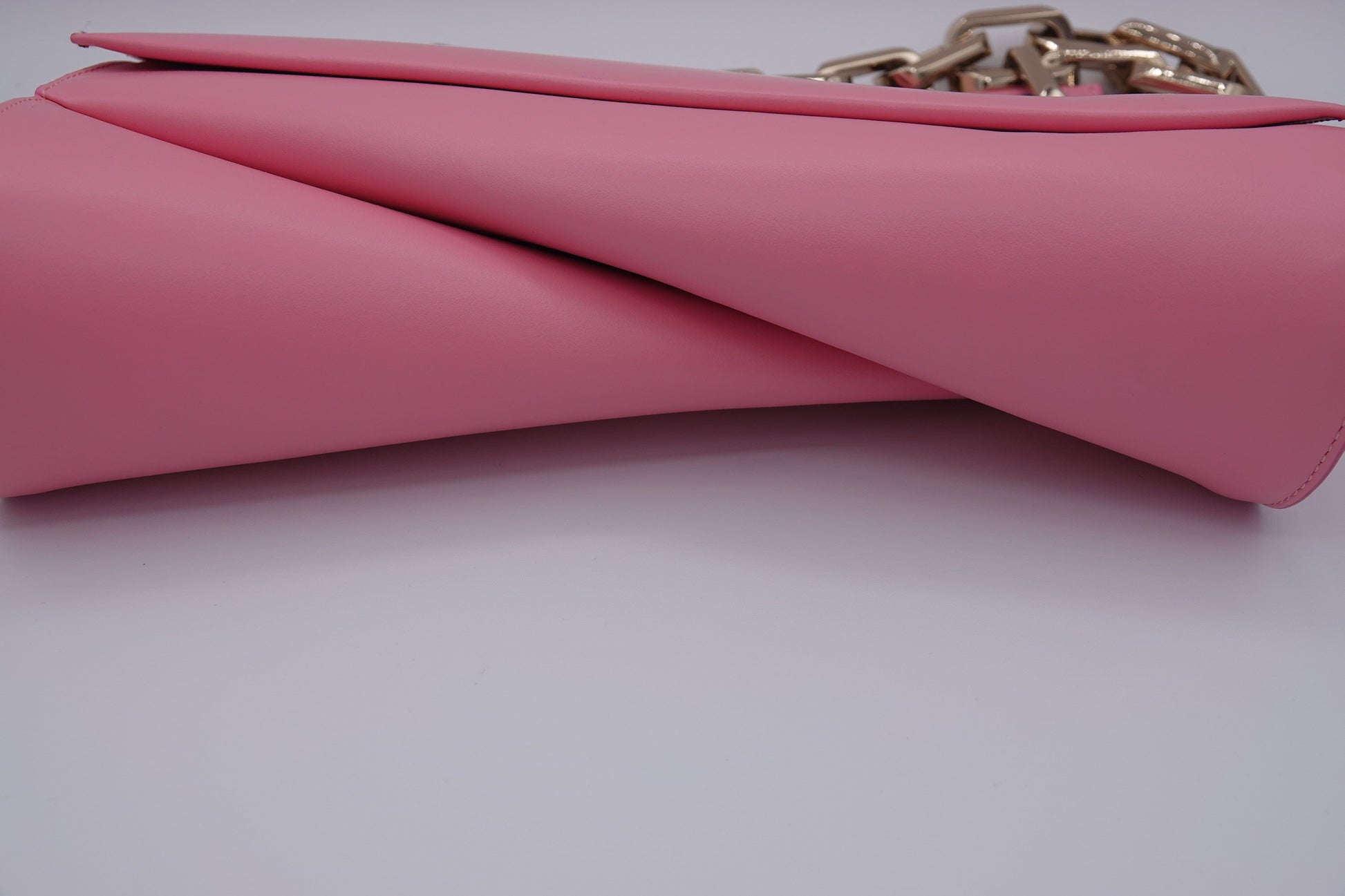 Pink clutch bag with a gold chain on a light gray background