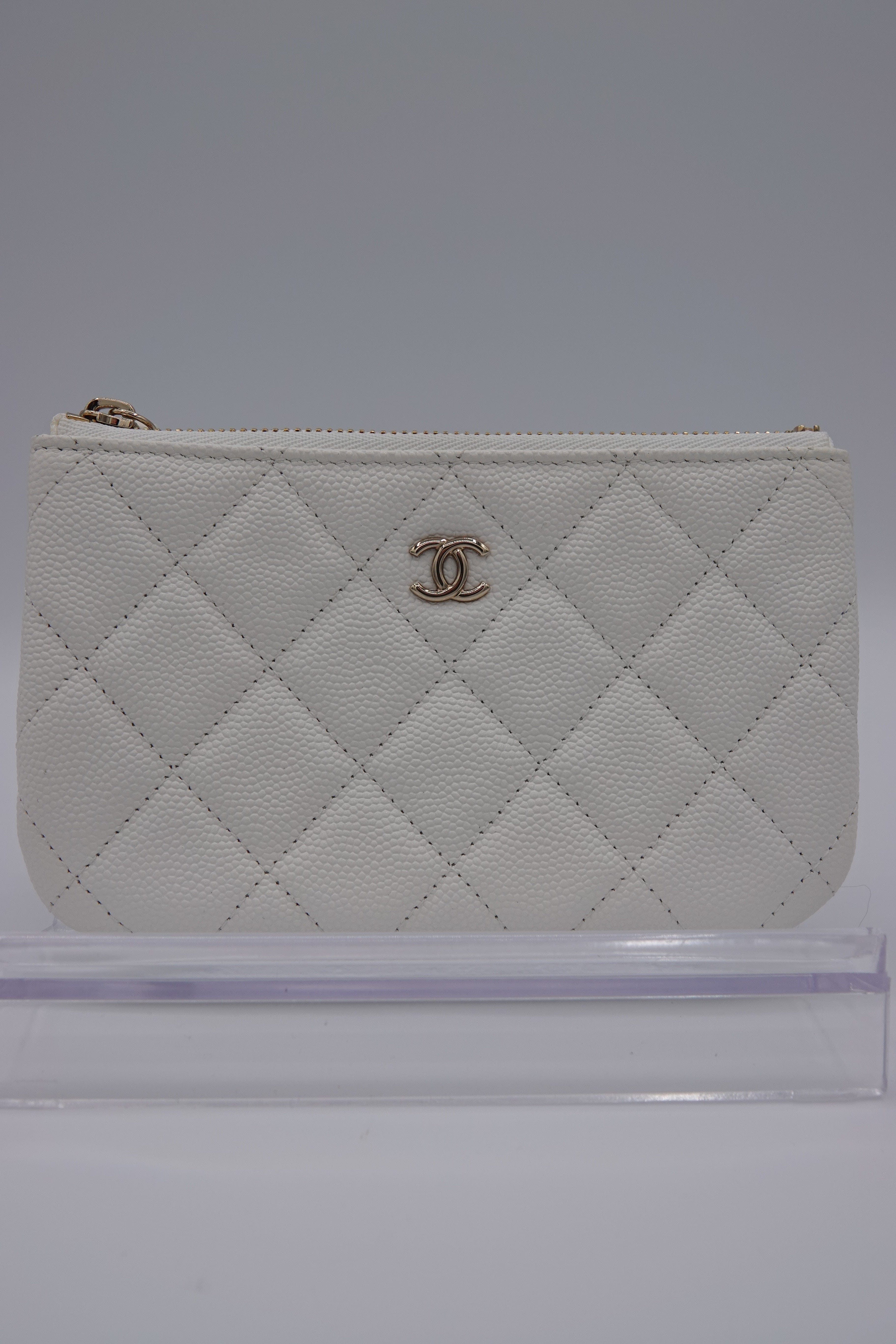 White quilted wallet with gold logo on a gray background