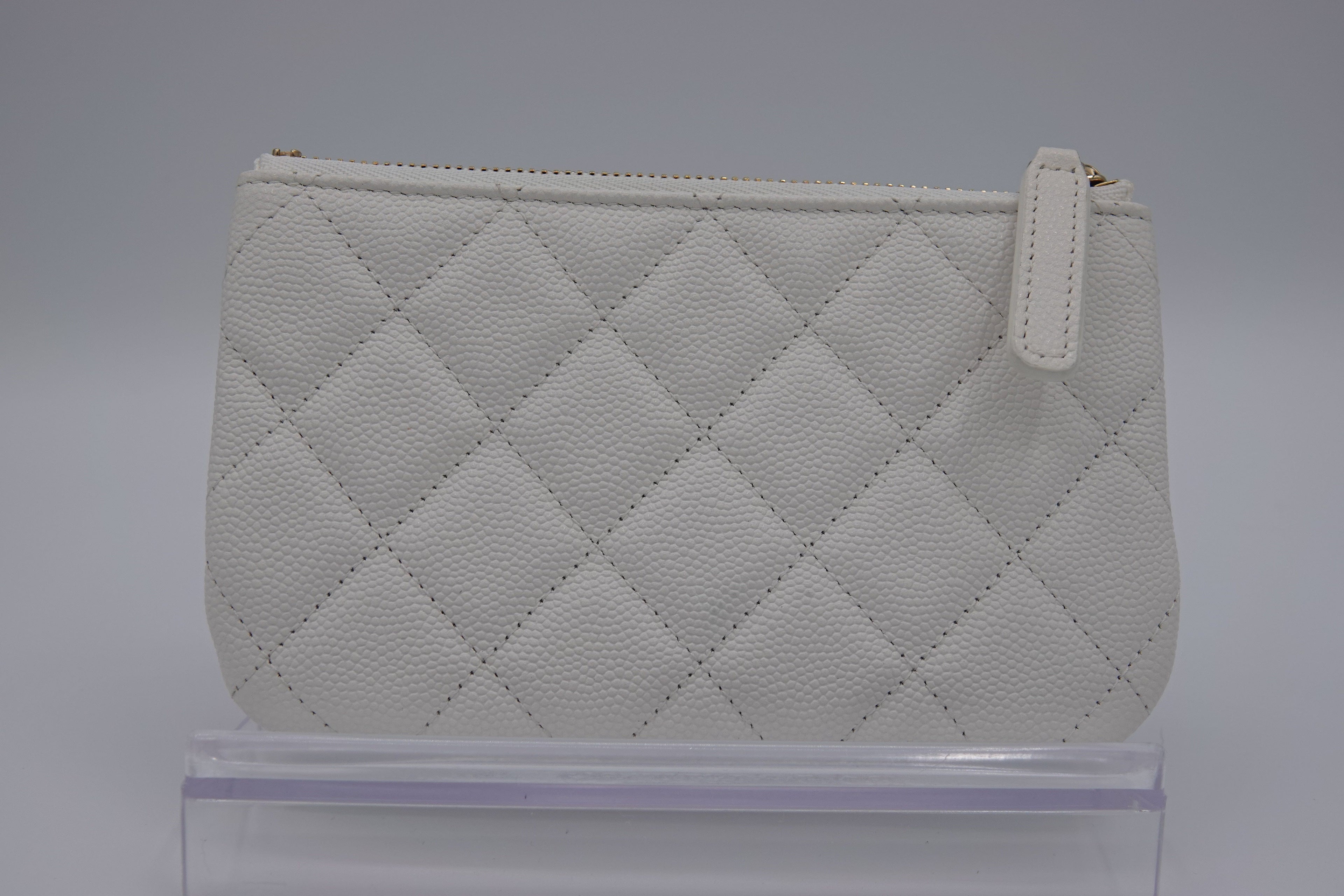 Quilted white pouch on a clear stand with a gray background
