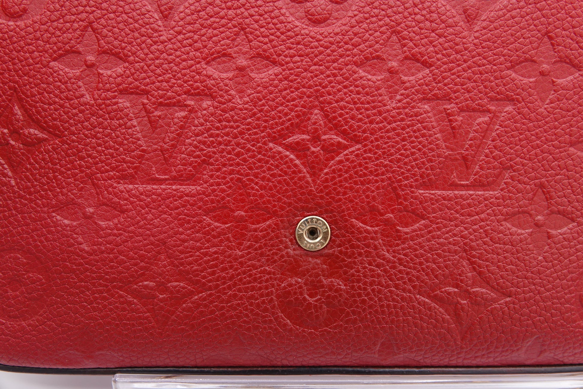 Close-up of a red leather handbag with a gold button, featuring the brand logo.