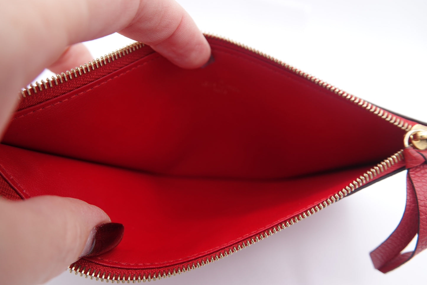 Red wallet with gold zipper held open by a hand on a white background