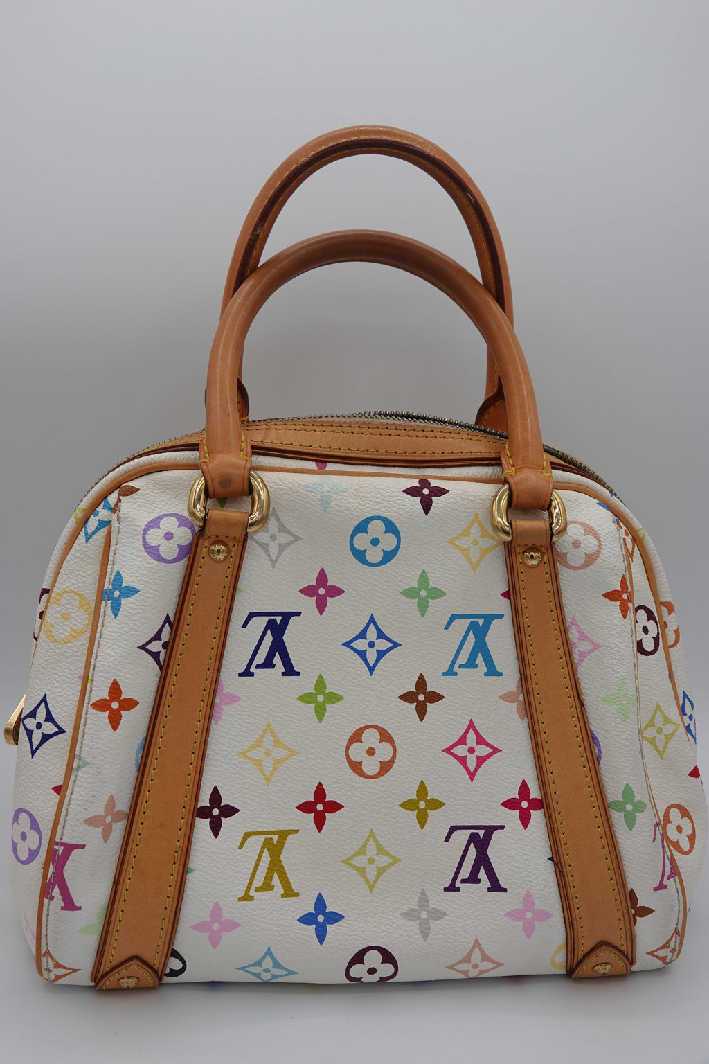 Designer handbag with multicolor logo pattern and brown leather handles on a light gray background