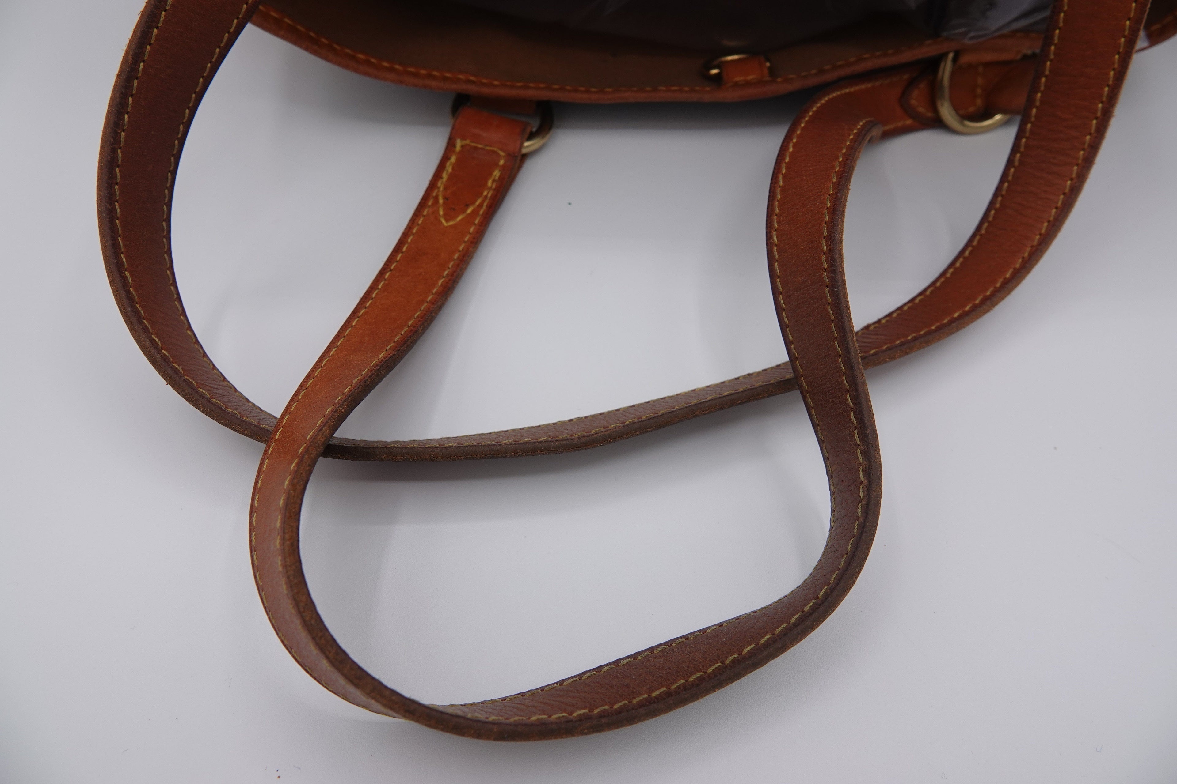 Close-up of a brown leather handbag with visible stitching on a white background