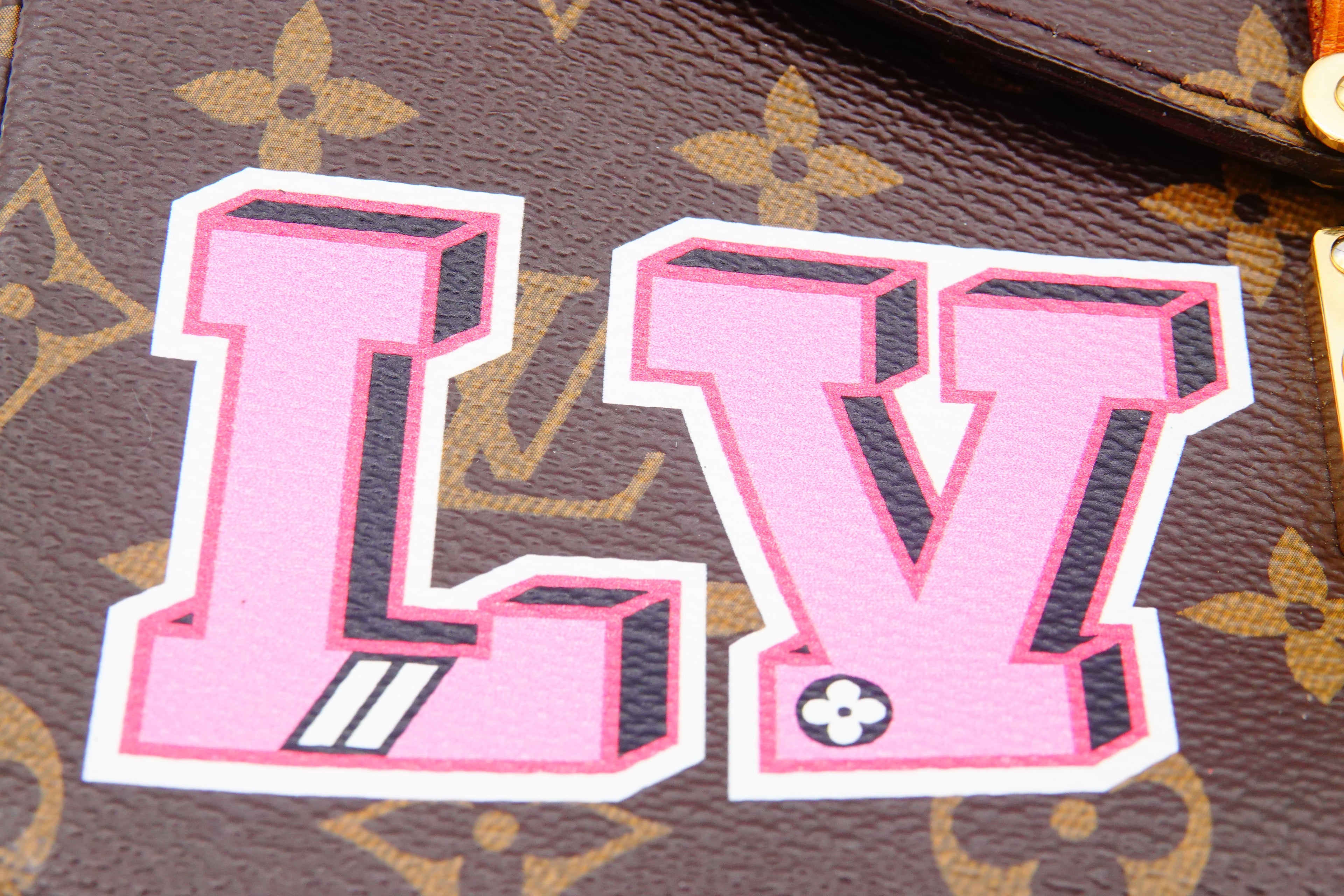 Pink 'LV' logo on a brown leather background with gold floral pattern