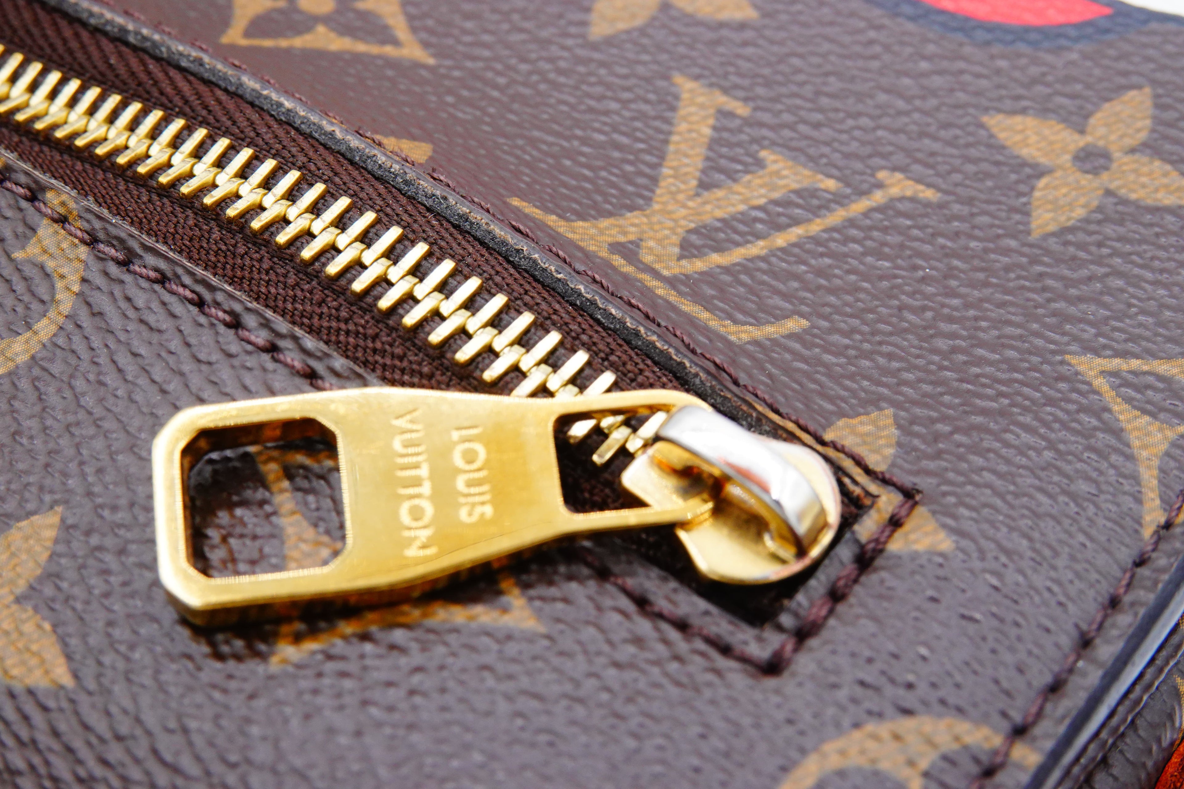 Close-up of a gold zipper on a Louis Vuitton bag with monogram pattern.