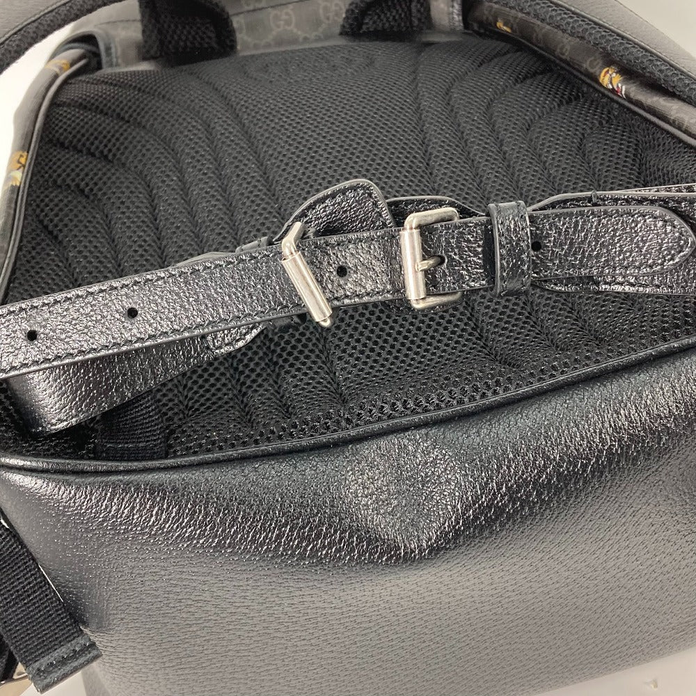 Close-up of a black leather bag with a strap and buckle on a textured surface.