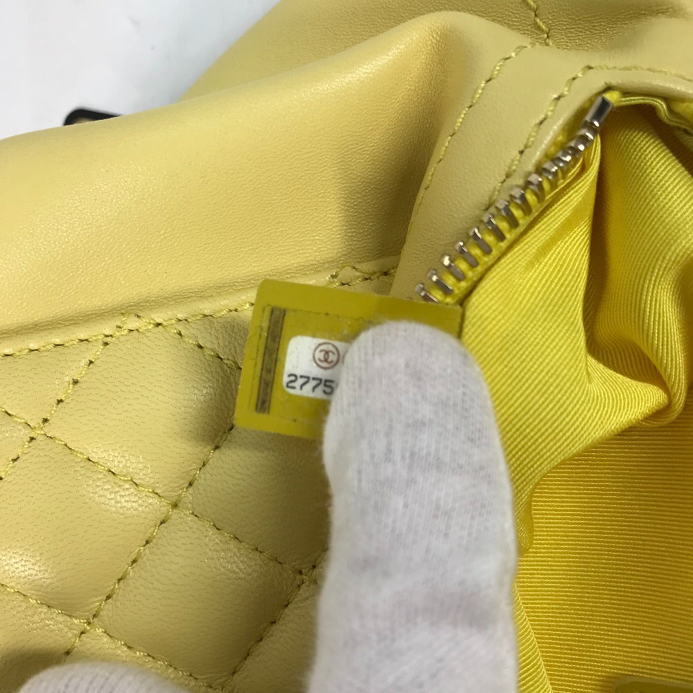 Yellow quilted handbag with a visible brand tag and white glove holding it open.