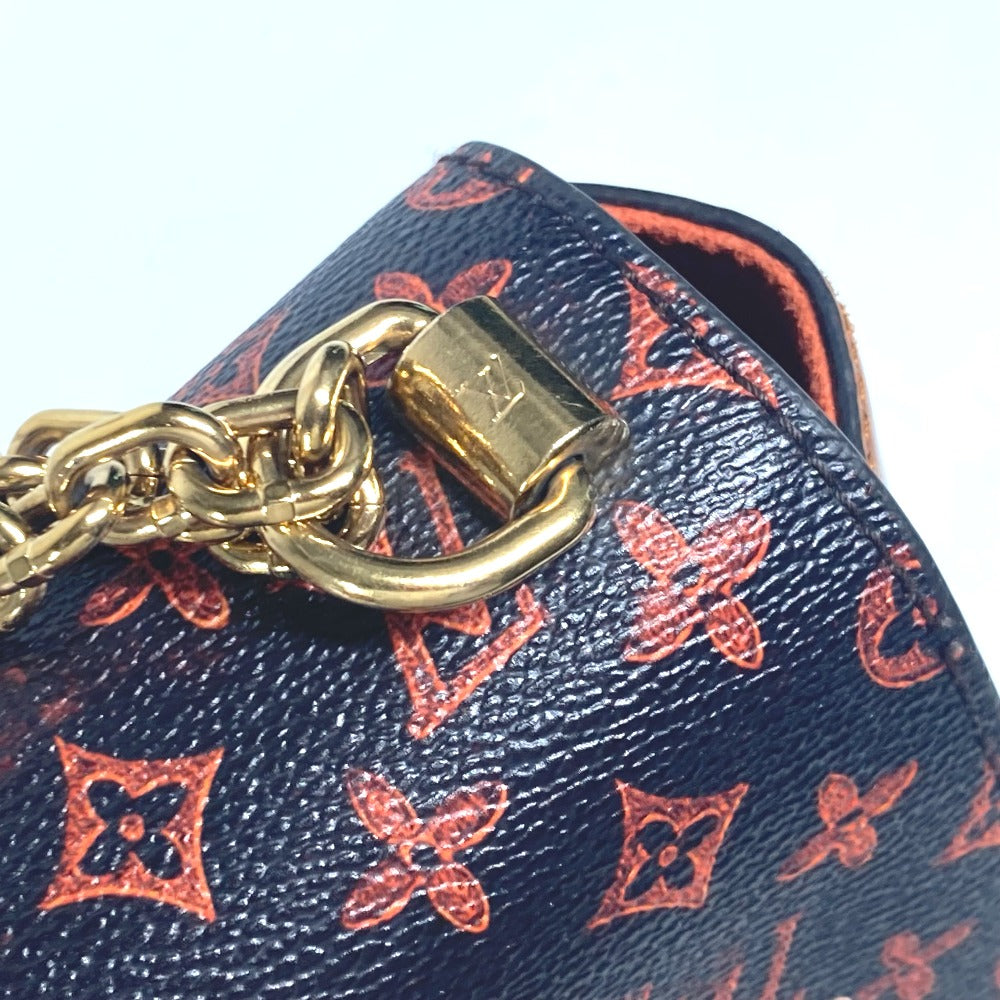 Close-up of a blue handbag with red monogram pattern and gold chain and lock detail.