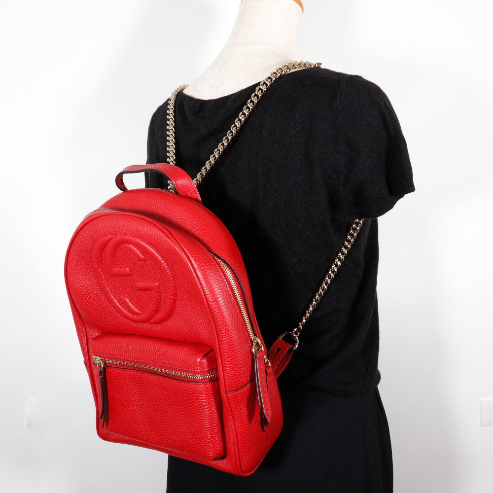 Red backpack with gold chain strap on a mannequin against a white background