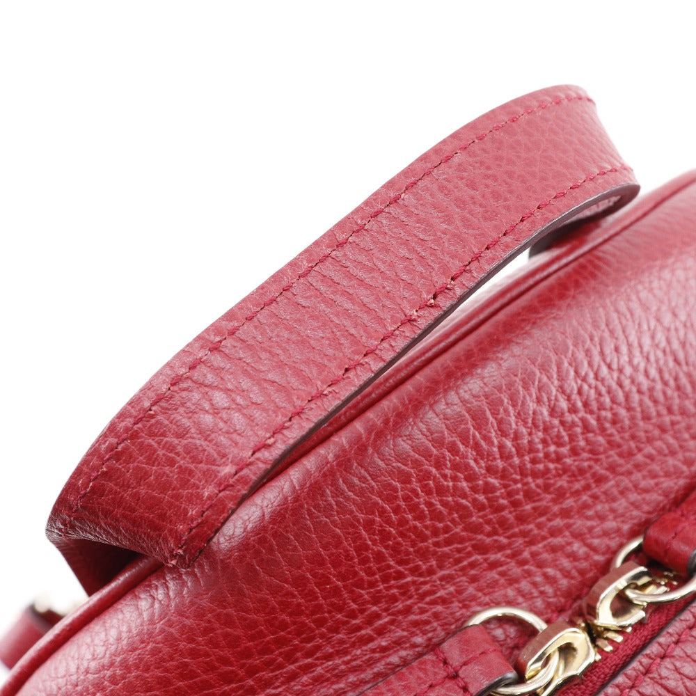 Close-up of a red leather handbag with a gold chain detail on a white background