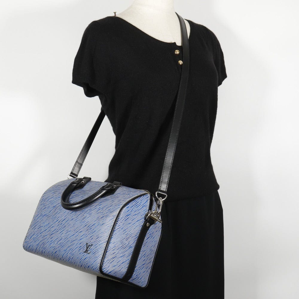 Blue handbag with black strap on a mannequin wearing a black dress against a white background